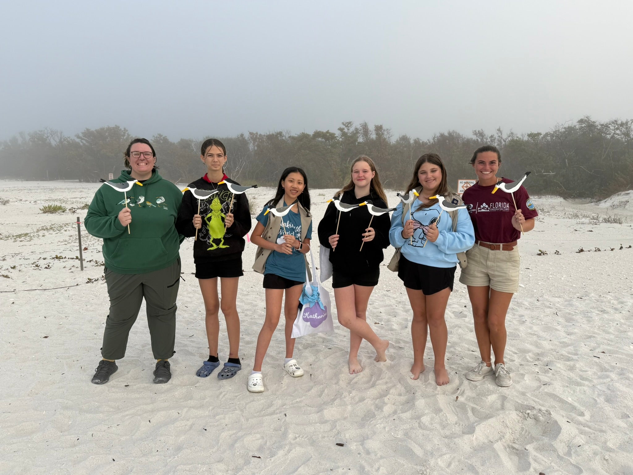 women holding least tern decoys and standing on a beach